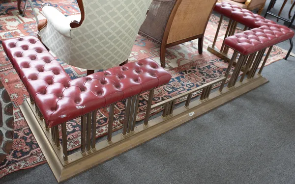 A Victorian style gilt metal and red faux leather club fender, with button back corner seats over square tubular rails and raised kerb, 216cm wide.