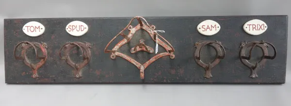 A wall mounted horse tack rack, by Martin Scorey, painted wood and metal, with a central driving harness mount flanked by four bridle racks, each with