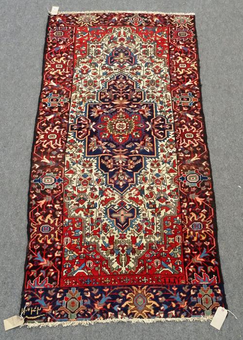 A Bakhtiari rug, reduced, Persian, the ivory field with an indigo medallion, madder spandrels, angular floral sprays, a black/indigo palmette border,