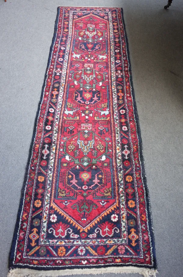 A North West Persian runner, the madder field with three stylised medallions, black spandrels, a black flower border, 298 x 82cm.