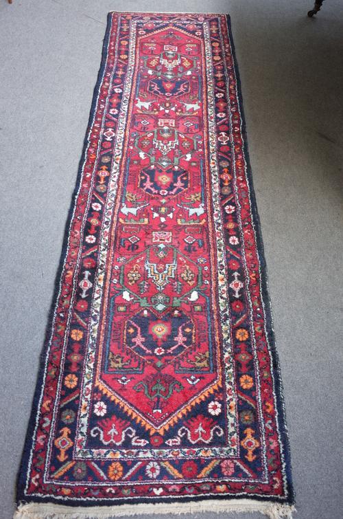 A North West Persian runner, the madder field with three stylised medallions, black spandrels, a black flower border, 298 x 82cm.