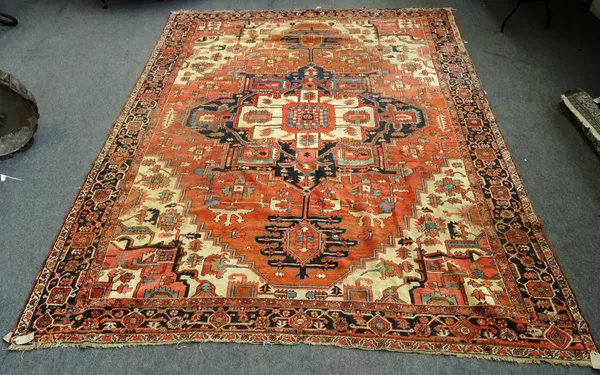 An Heriz carpet, Persian, the madder field with a bold angular pole medallion, ivory spandrels, all with angular flowers sprays, a black palmette and