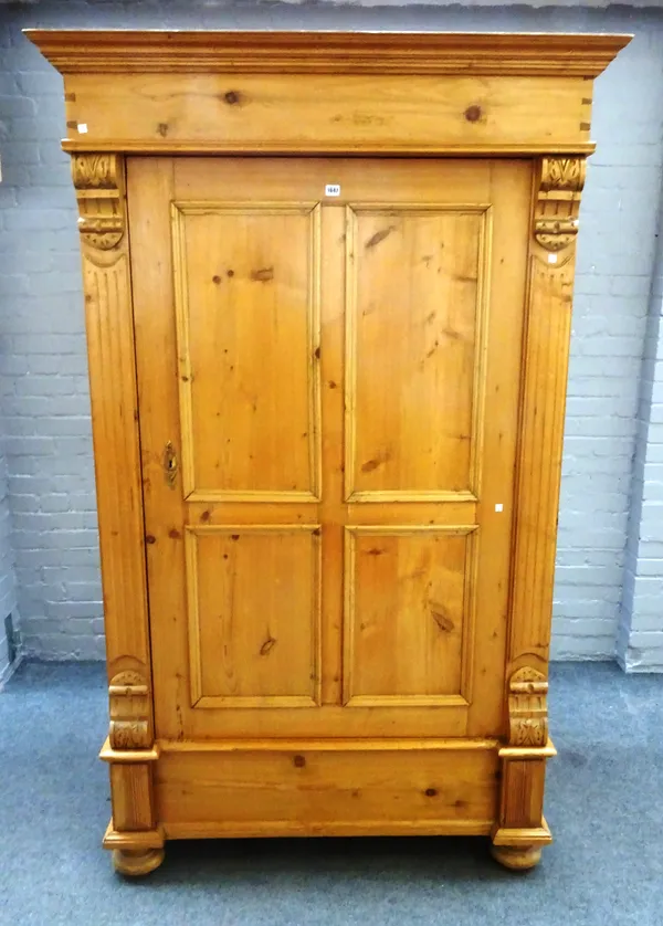 An early 20th century pine armoire with single door flanked by fluted pilasters on bun feet, 127cm wide x 208cm high x 68cm deep.