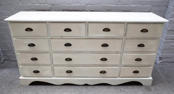 A 20th century off-white painted pine chest of thirteen various drawers, on shaped plinth, 167cm wide x 85cm high x 40cm deep.