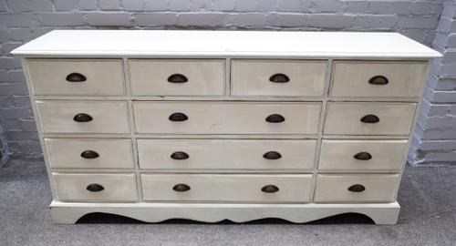 A 20th century off-white painted pine chest of thirteen various drawers, on shaped plinth, 167cm wide x 85cm high x 40cm deep.