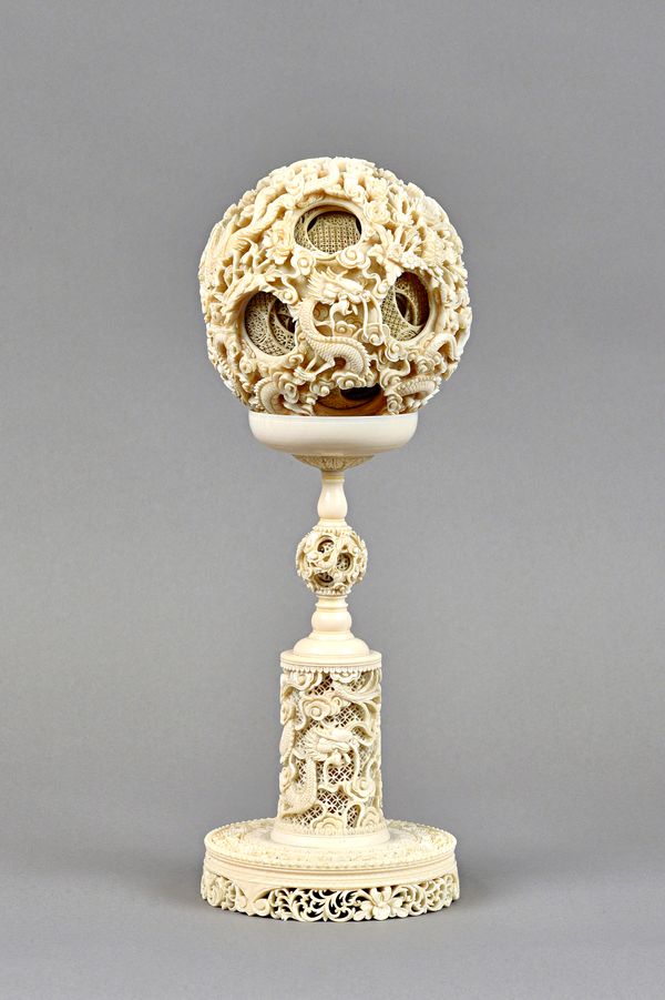 A Chinese ivory puzzle ball and stand, early 20th century, the ball carved and pierced on the exterior with dragons and cranes amongst cloud scrolls,