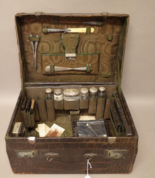 A crocodile travelling toilet case, containing a part set of silver mounted glass bottles and jars, manicure implements, a pair of glove stretchers, a