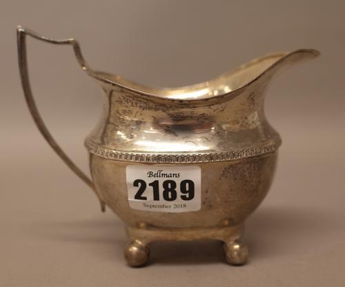 A silver milk jug, of helmet shaped form, having a reeded handle, decorated rim and raised on four spherical feet, Birmingham, the date letter rubbed,