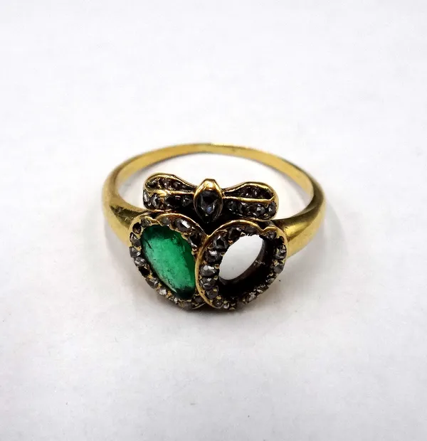 A gold, emerald and diamond ring in a twin hearts and bow design, mounted with a pear shaped emerald and with rose cut diamonds, (one coloured gemston
