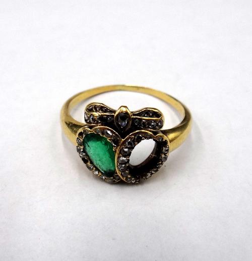 A gold, emerald and diamond ring in a twin hearts and bow design, mounted with a pear shaped emerald and with rose cut diamonds, (one coloured gemston