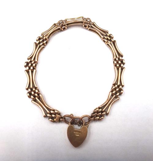 A gold curved bar and oval link gate bracelet, detailed 15 CT, on a gold heart shaped padlock clasp, detailed 15 C, weight 13.5 gms.