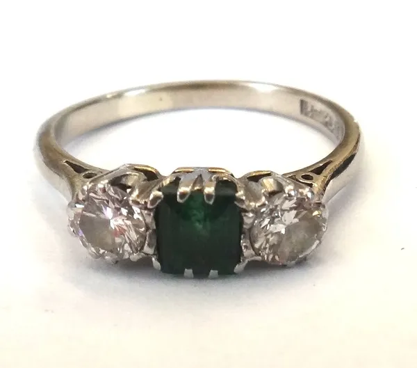 A white gold and platinum, emerald and diamond three stone ring, claw set with the square cut emerald at the centre, between two circular cut diamonds