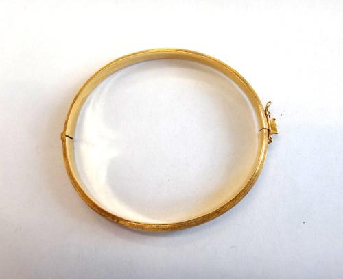 A gold oval hinged bangle, having a textured finish, on a snap clasp, with a foldover safety catch, gross weight 11.6 gms.