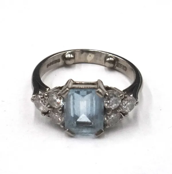 An 18ct white gold, aquamarine and diamond ring, claw set with the cut cornered rectangular step cut aquamarine between circular cut, diamond set thre