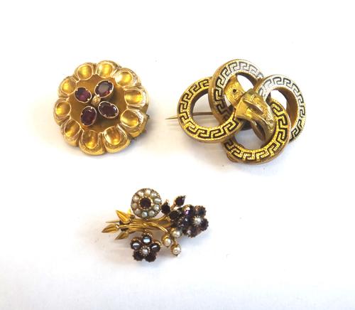 A garnet set shaped circular brooch, mounted with four oval cut garnets, the back glazed with a locket compartment, a Victorian black enamelled brooch