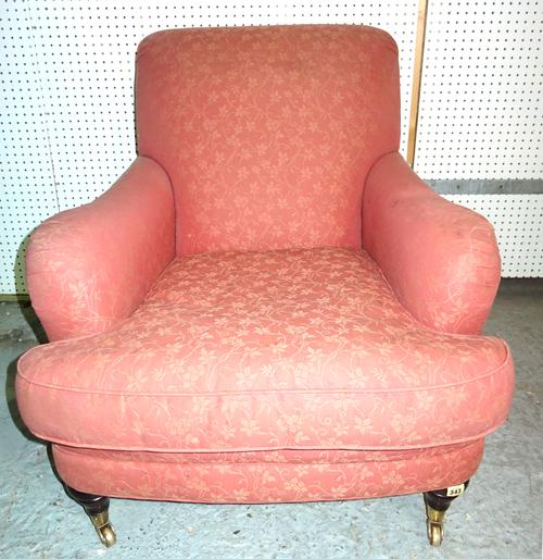 A modern club armchair, with red foliate upholstery on turned wooden supports and brass castors.  BAY 1