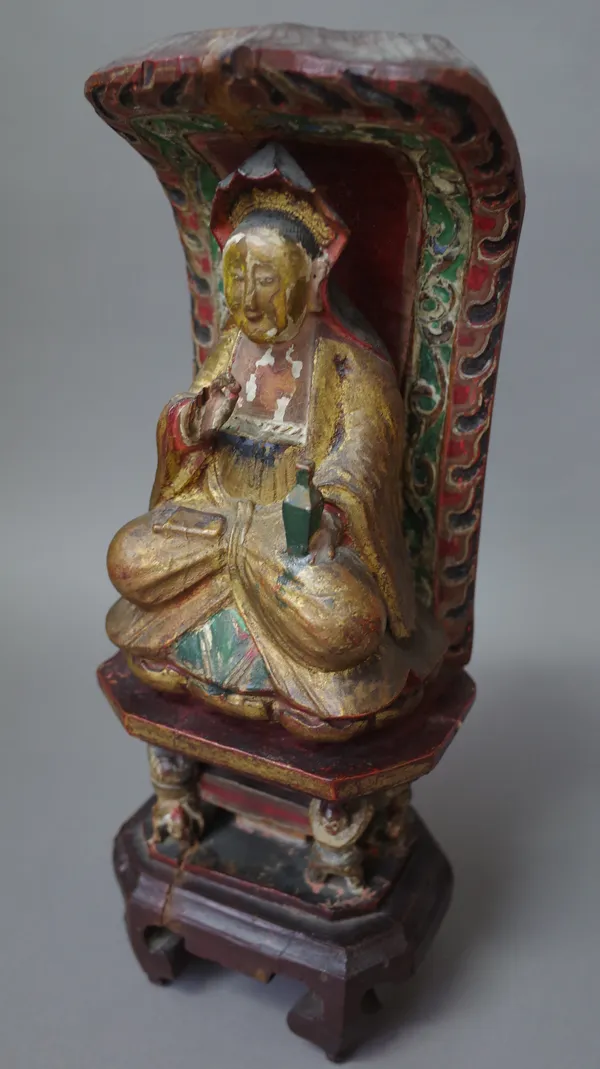 A Chinese polychrome carved wooden Buddha figure, late 19th century, modelled in completive pose on a shrine with text to the rear, 36cm high.