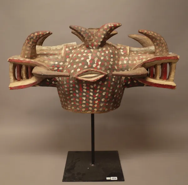 A Senufo tribal wooden two headed mask on stand, polychrome painted with red and white spotted decoration, displayed on a purpose made metal stand, ma