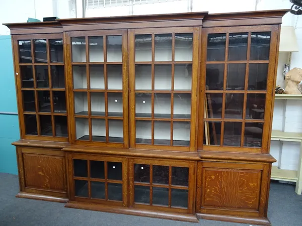 In the manner of Heals; an Arts & Crafts oak breakfront library bookcase, with four glazed doors, the base with central glazed door flanked by panel c