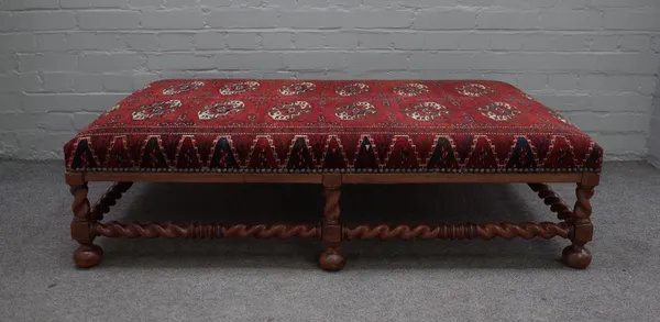 A large rectangular footstool with carpet upholstery, on walnut barleytwist supports, 130cm wide x 35cm high.