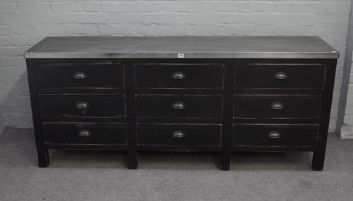 A zinc topped side cabinet, the ebonised base with three rows of three drawers, 182cm wide x 77cm high.