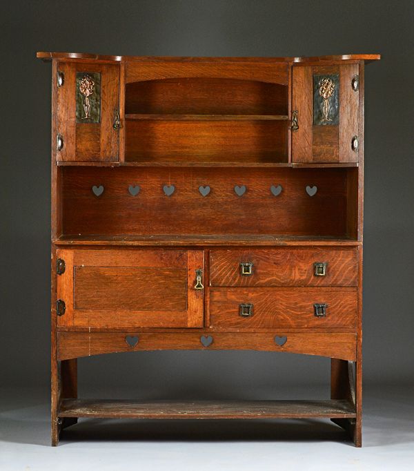 An Arts & Crafts oak dresser with pierced heart and embossed copper floral panels on pierced slab ends, 151cm wide x 176cm high. Illustrated.