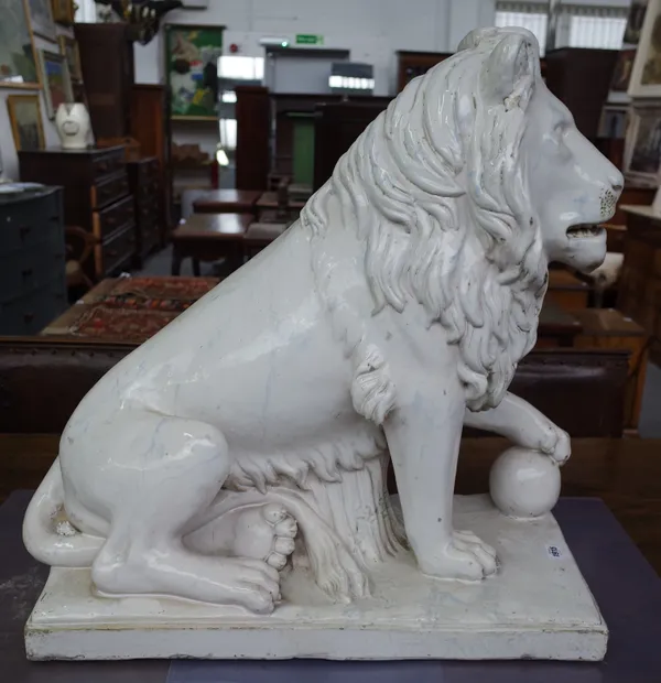 A large Portuguese white faience figure of a lion, 20th century, modelled seated on its haunches with left paw resting on a ball, its fur picked out i