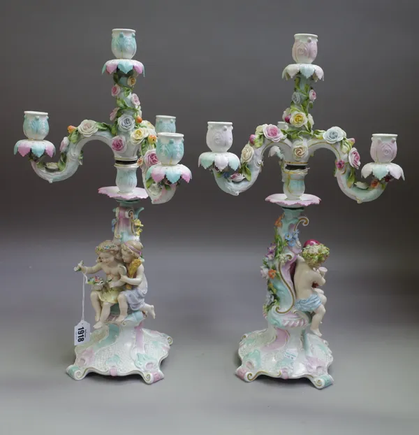 A pair of Sitzendorf four-light candelabra, circa 1900, each modelled with two putti representing a season, seated against a column beneath three scro