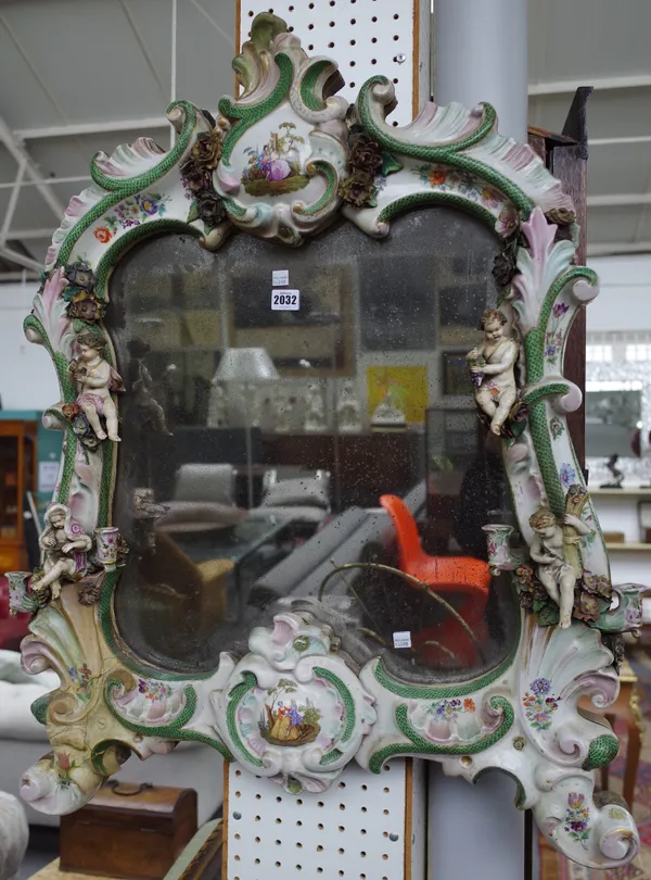 A large German porcelain mirror, late 19th century of Rococo form, painted with flowers and vignettes of lovers in a landscape applied with four putti