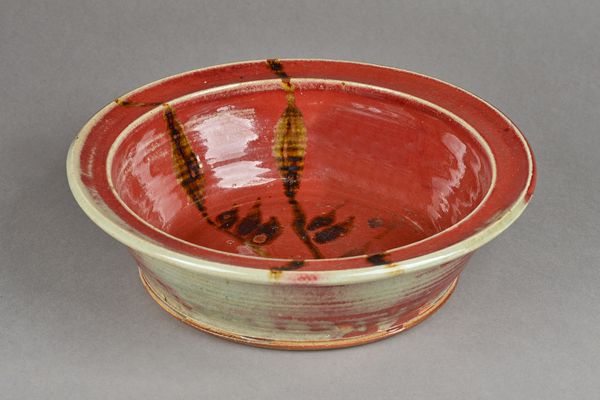 Clare Sutcliffe (1943-2019), a rimmed bowl with reed design and copper red glaze, makers mark, 32cm diameter. Illustrated.