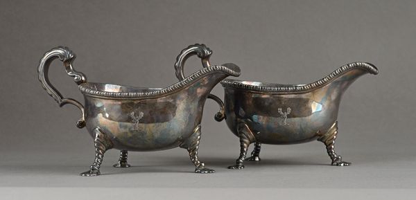 A George II pair of silver sauceboats, each decorated with a beaded rim, scrolling handle and raised on three pad feet, crest engraved, London 1750, m