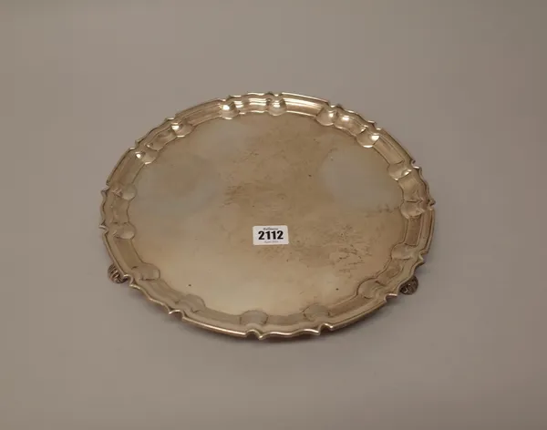 A silver salver, of shaped circular form, having a pie-crust rim, crest engraved to the centre and raised on three scrolling feet, in the Chippendale