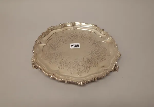 A Victorian silver salver, of shaped circular form, having a decorated pie crust rim, otherwise with floral engraved decoration and raised on three pi