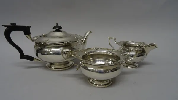 A silver three piece tea set, comprising; a teapot having black fittings, a twin handled sugar bowl and a milk jug, each piece of compressed circular