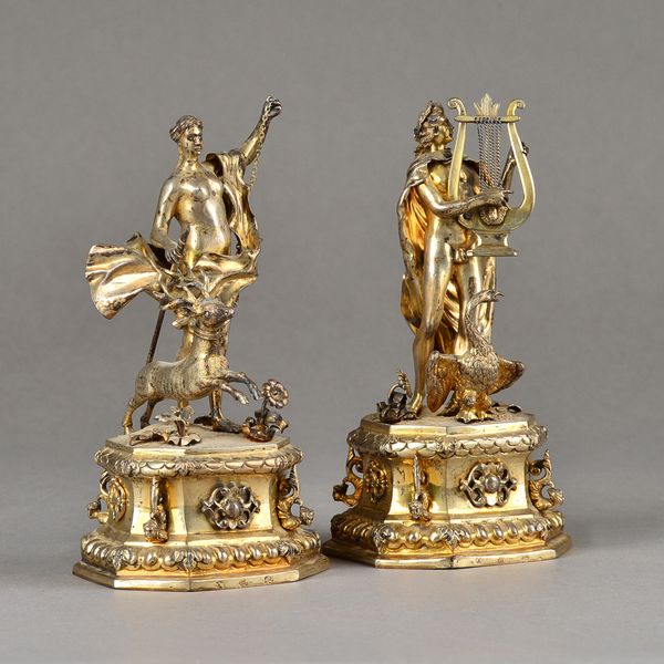 Two similar European gilt figures of classical deitys, one with a spear and a stag and the other with a lyre and a swan, raised on a cartouche shaped