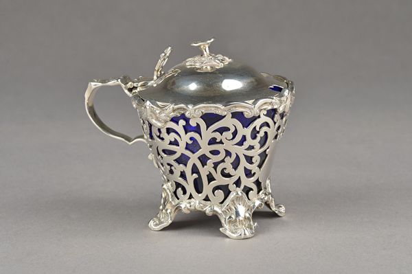 A Victorian silver mustard pot, of tapered form, with scroll pierced decoration within cast borders, the hinged lid with a flower finial, Birmingham 1