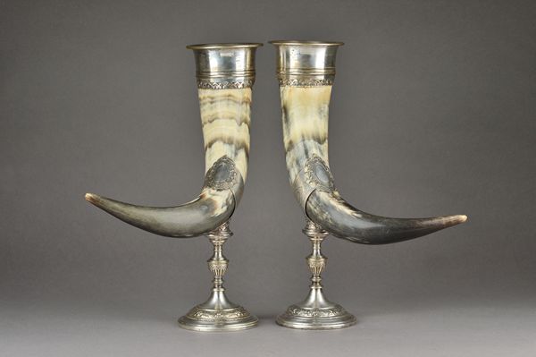 A pair of silver plated metal mounted horn table ornaments, each with scroll and floral decoration to the mounts and raised on a weighted circular bas