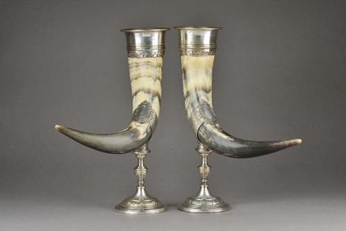 A pair of silver plated metal mounted horn table ornaments, each with scroll and floral decoration to the mounts and raised on a weighted circular bas