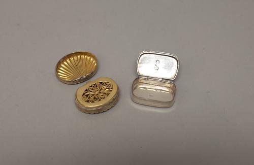 A silver vinaigrette of scallop shell form, Birmingham possibly 1805, the hinge to the lid damaged and a silver curved rectangular hinge lidded pill b