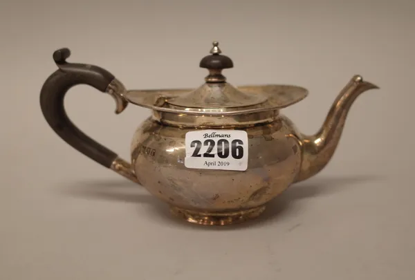 A silver teapot, of squat oval form, with black fittings, raised on a circular foot, London 1912, gross weight 244 gms.