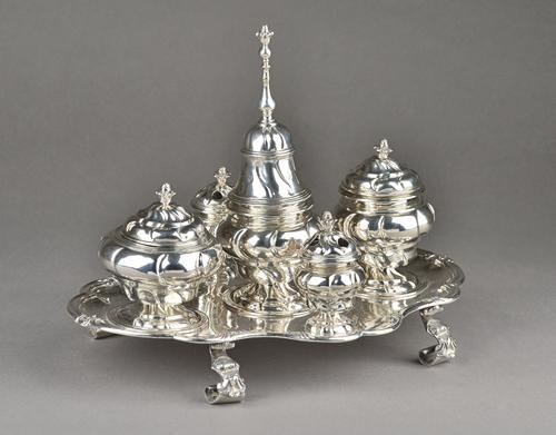 A Spanish inkstand, of shaped oval form, having a bold scrolling border, raised on four bold Rococo feet, the central sander with a bell form cover, t