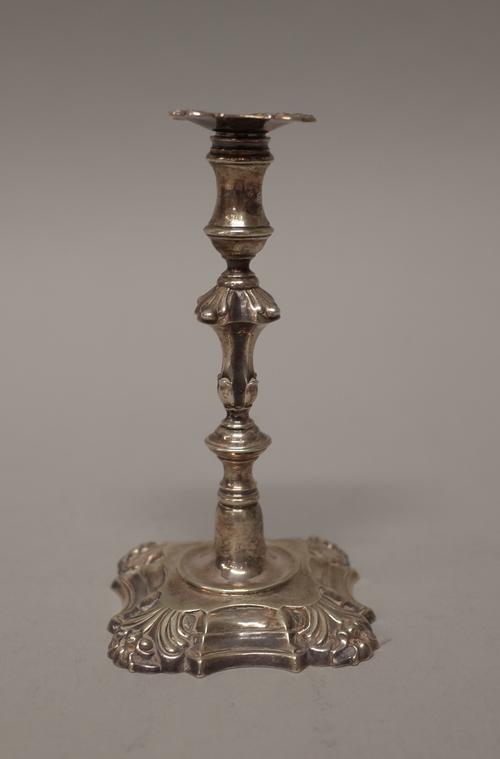 A silver taper stick decorated with a knopped stem raised on a shaped square base with partly fluted corners, London mid 18th century (hallmarks indis