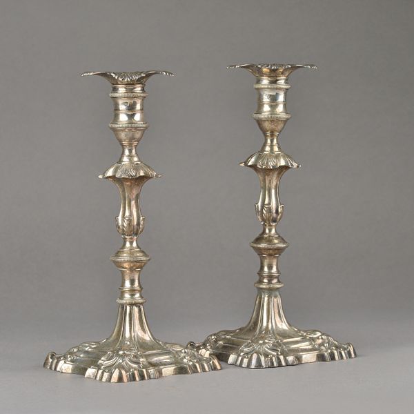 A pair of late George II silver table candlesticks, each of cast form, with a knopped stem, on a shaped square base decorated with scalloped corners,