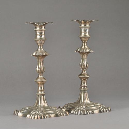 A pair of late George II silver table candlesticks, each of cast form, with a knopped stem, on a shaped square base decorated with scalloped corners,