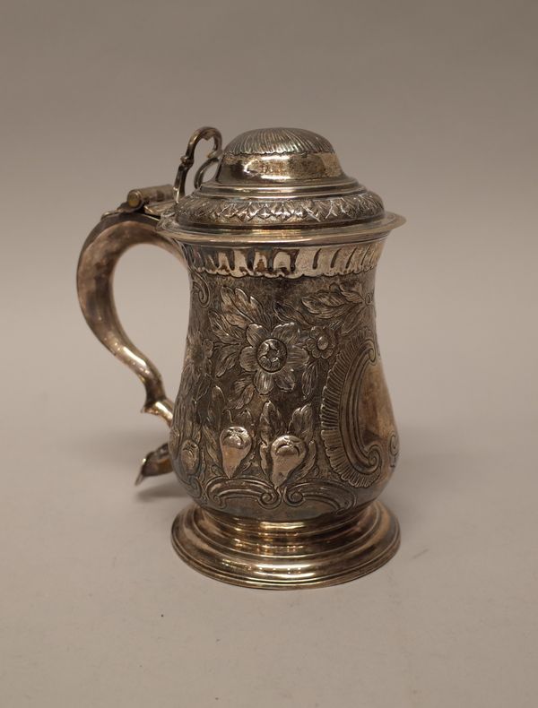 An early George III silver hinge lidded tankard, the baluster shaped body later embossed with floral, fruit and scrolled decoration, the scrolled hand