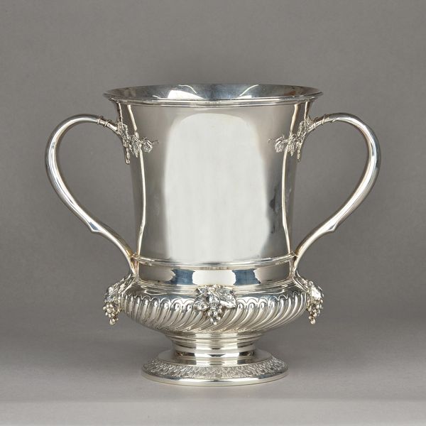 A Tiffany & Co Sterling silver twin handled cup, the handle mounts and the spiral fluted band to the body decorated with fruiting vine, raised on a ci