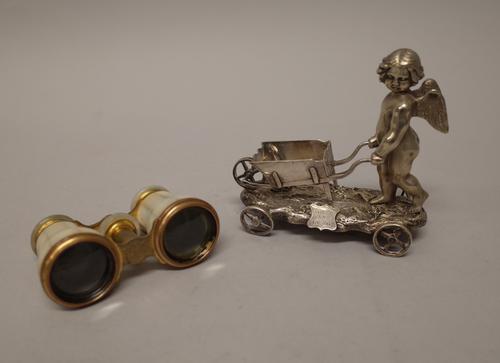 A silver plated model of a cherub, with a wheelbarrow, on a rustic base, fitted with four wheels and a pair of gilt metal mounted mother-of-pearl oper
