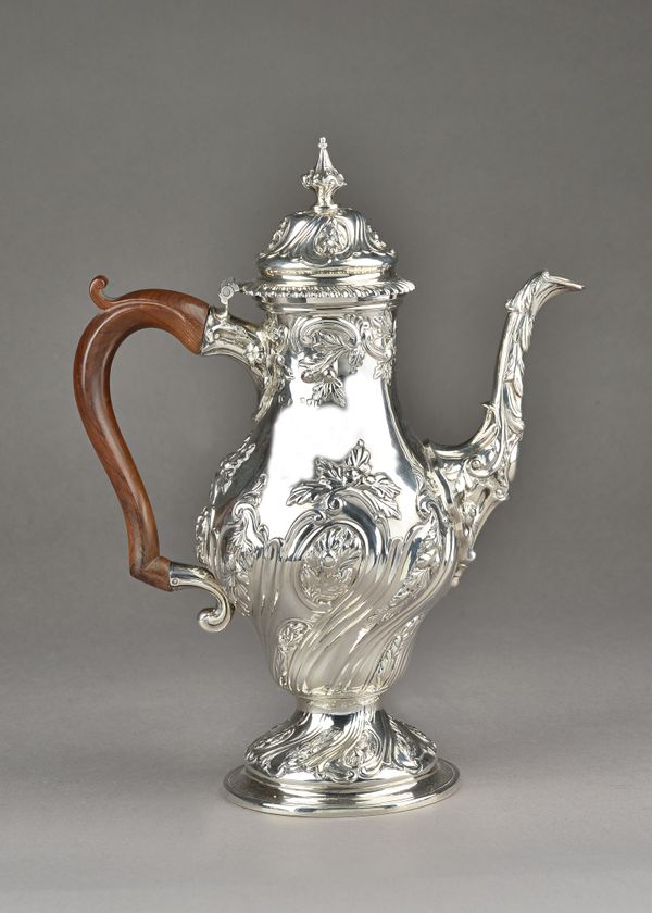 A late George II silver coffee pot, of baluster form, embossed with spiral foliate sprays within fluted divisions, the hinged lid with a cast finial a