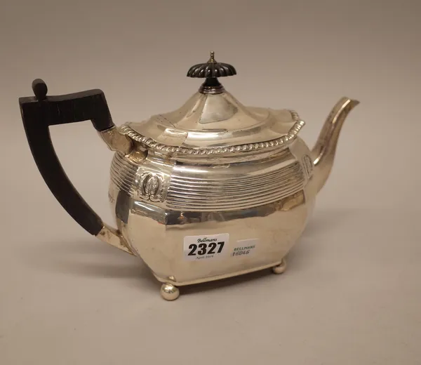 A silver teapot of panelled oval form, decorated with a reeded band below a gadrooned rim, raised on four spherical feet, with black fittings, London