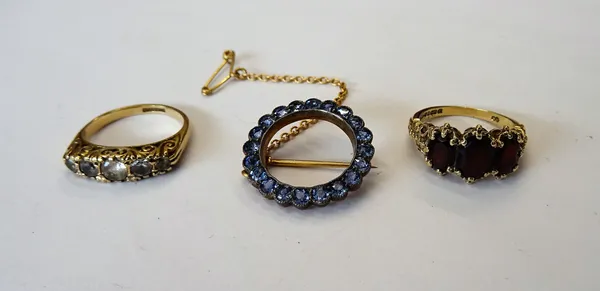 A sapphire brooch of circular openwork form, mounted with pale blue sapphires, a 9ct gold and garnet set three stone ring, mounted with oval cut garne